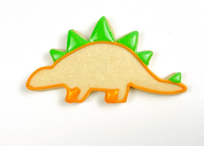 Image of Once the orange outline is relatively dry, use green piping consistency icing to outline the spikes on the spine of the stegosaurus. Fill these outlines with flood-consistency green royal icing.