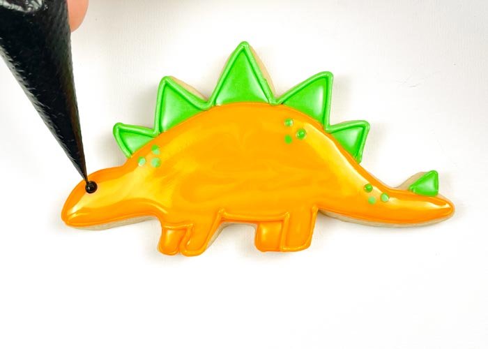 Image of Using black piping consistency royal icing, pipe a small dot to create an eye for your dino. If you want to skip mixing up a batch of black icing, you can also use a small candy or nonpareil to create the dinosaur eye. 
