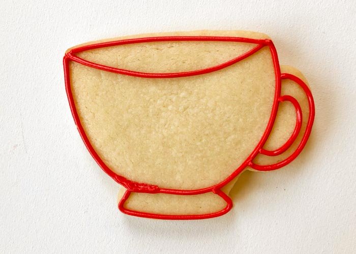 Image of Outline the three sections of the teacup as shown with red piping consistency icing: the main part of the cup, the base, and the handle. Also create definition around the rim of the cup as shown. You can pipe some squiggles of red piping consistency icing in the body of the cookie, this will help your flood icing to set up nicely and prevent it from collapsing.