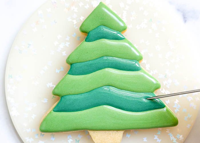Image of Fill in these small sections with dark green flood consistency icing and smooth out as needed with your scribe tool or toothpick, coaxing out any air bubbles and ensuring full coverage of the cookie.