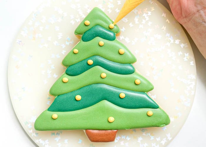 Image of Using the yellow detail consistency icing, pipe dots scattered all over the tree. Leave room for the red dots. You can also use sprinkles at this step--we recommend large sugar pearls to go with this fun design.