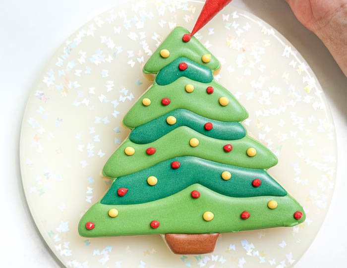 Image of Using the red detail consistency icing, pipe dots scattered all over the tree. These simple and sweet Christmas Tree cookies are a joy to decorate. The two color tones add some depth to the design, and you can decorate and embellish as desired. 