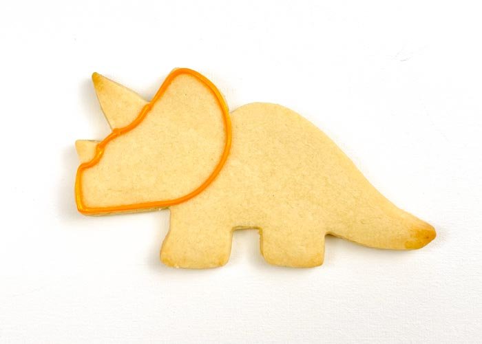 Image of Using piping consistency orange icing, outline your shape. First, pipe the head, leaving the horns bare. Next, pipe the rest of the body. Pipe small rectangles in the legs to create 4 legs for your dino.