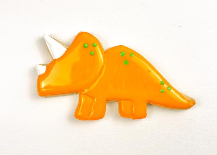 Image of While the flood icing is still wet, use piping consistency green royal icing to pipe dots to give your dino some detail. Doing this step while your green flood icing is still wet will ensure that the details look like they are part of the dino, rather than standing out on the body of the dino. If you prefer more dimension, you can wait for your flood icing to dry 30-60 minutes before piping the details.
