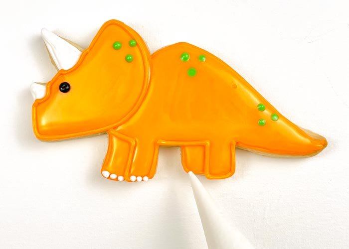 Image of Using white piping consistency royal icing, pipe dots on the bottom of the legs to create cute little toes for your dino. 