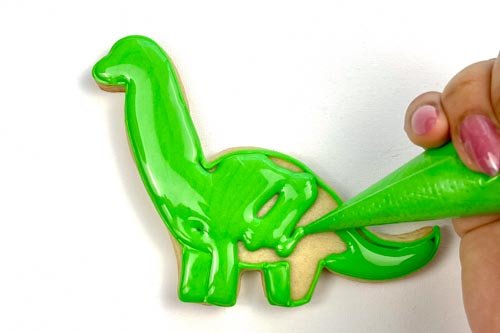 Image of Using piping consistency green icing, pipe some squiggles in the body of the brontosaurus. This will help to give your flood some structure, so that the icing doesn't collapse as it cools.
