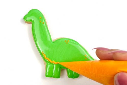 Image of To create some detail in the belly, pipe orange piping consistency icing on the underside of the dino, then use a scribe tool to create swirls & blend the belly area into the rest of the dino.