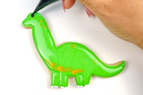 Image of Using black piping consistency royal icing, pipe a small dot to create an eye for your dino. If you want to skip mixing up a batch of black icing, you can also use a small candy or nonpareil to create the dinosaur eye. And you're done! 