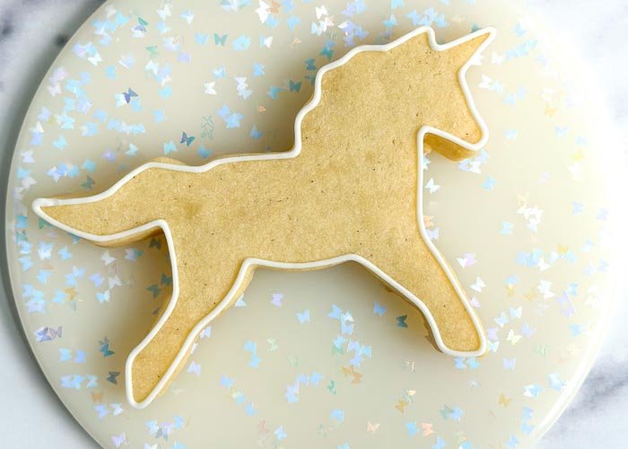 Image of Outline the entire cookie in white piping consistency royal icing. Pipe a squiggle of white piping consistency icing in the body of the unicorn, this will prevent the flood consistency icing from collapsing or cratering. Move immediately to the next step.