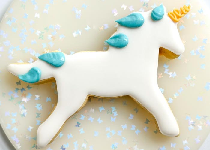 Image of Using the blue piping consistency royal icing, pipe the unicorn mane as shown in the photo. Use the tip of your bag to create a swooping look to the mane-it will add to the jumping motion of the unicorn. Dispense royal icing with the tip of your piping bag pressed firmly on the cookie, then remove in a sweeping motion to get some movement in the mane. Pro tip: It can be helpful to cut a larger hole than you would typically use for piping consistency so that you don't have to add more pressure to the bag and get a smoother effect to the icing. Let the icing dry for 30-60 minutes.