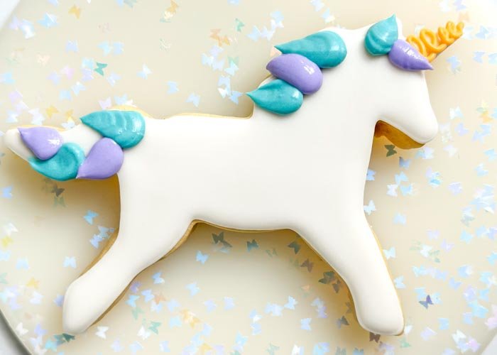 Image of Using the purple piping consistency royal icing, pipe the unicorn mane next to the blue icing you just piped. Let the icing dry for 30-60 minutes.