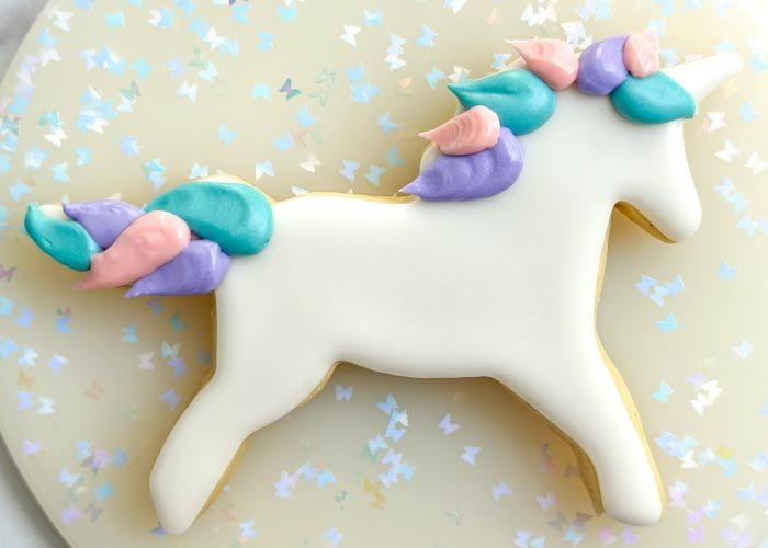 Image of Using the pink piping consistency royal icing, pipe the unicorn mane next to the purple icing you just piped. Let the icing dry for 30-60 minutes.