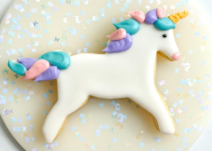 Image of Using the black outline consistency royal icing, pipe a small dot for the unicorn eye. Alternatively, you can use a small candy for the eye. Using the pink piping consistency royal icing, pipe the nose and use your scribe tool or toothpick, to smooth out the icing. 