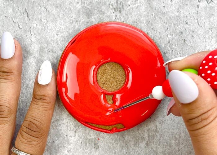 Image of Use your red flood consistency to fill in the O, leaving the center bare. Use a scribe tool or toothpick to gently move the icing around. This will ensure full coverage of the cookie and will also get rid of any air pockets in your icing.