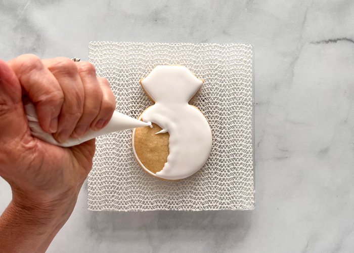 Image of Next, flood the entire cookie with white flood icing. Use a scribe tool or toothpick to coax the icing around. This will also pop any air bubbles in the icing. 