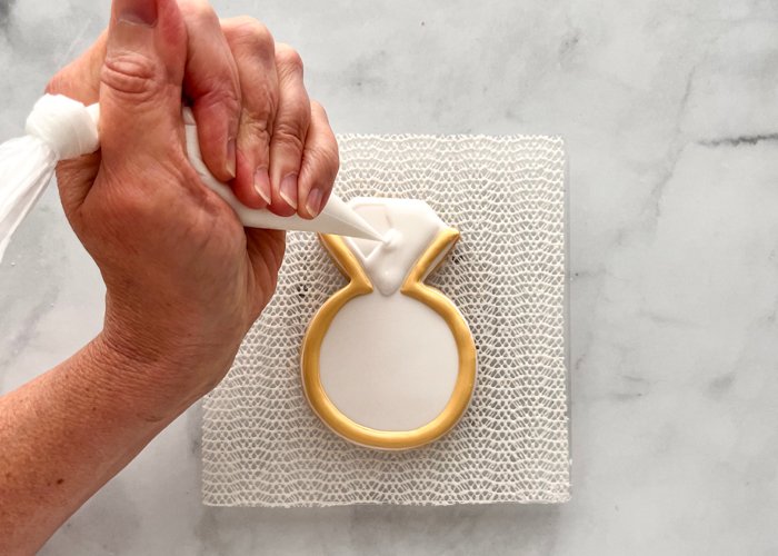 Image of Using white piping consistency icing, outline the shape of the diamond between the two prongs. Fill with flood consistency white icing, and allow to dry until just crusting over. If you are opting to paint the band gold, go to the next step. If you'd prefer to leave the band a deep yellow-gold color without metallic luster, skip to step 7.