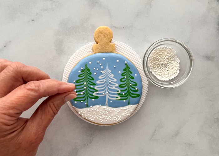 Image of Add more nonpareils to the blue area and trees to give a layered effect and the look of a true snow globe.