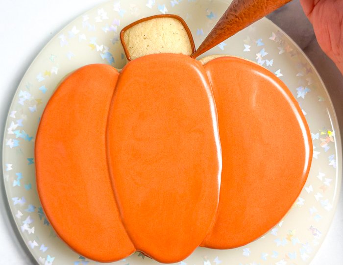 Image of Outline the stem of the pumpkin with the brown piping consistency icing. Pipe a squiggle of the same icing in the middle of the stem.