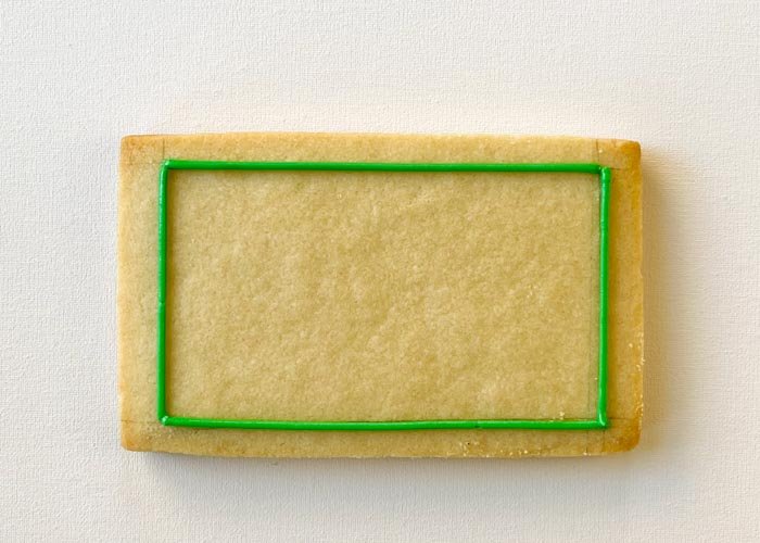 Image of Using piping consistency green icing, outline the blackboard, leaving a border around the edge.