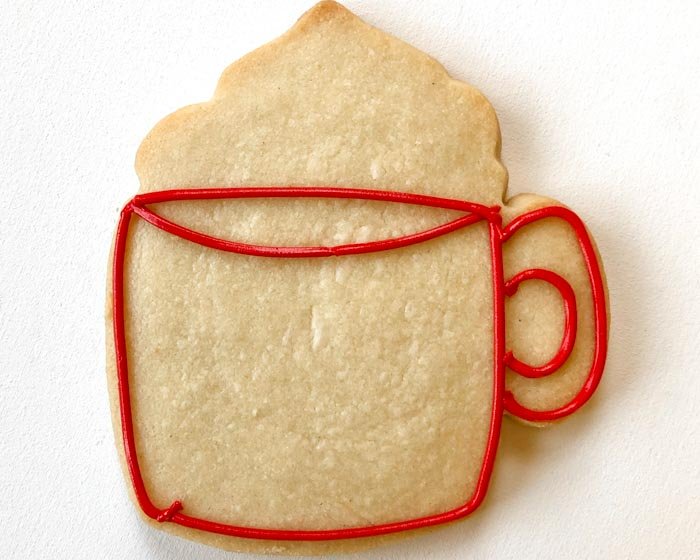 Image of Outline the shape of the mug with red piping consistency icing. Be sure to outline the rim of the mug and the handle of the mug as shown.