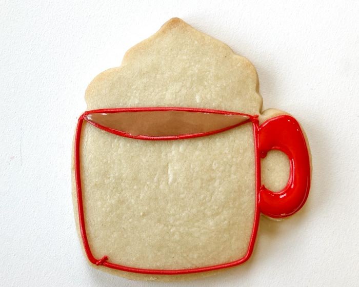 Image of Using red flood consistency icing, fill the handle of the mug. Use a toothpick or scribe tool to ensure full coverage and to eliminate any air bubbles in your icing. Wait for the red flood icing to dry until just crusting over, 30-60 minutes. While waiting for the red handle to dry, flood the top of the mug with brown flood consistency icing.