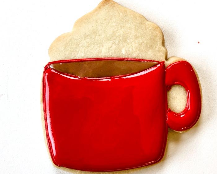 Image of Once the brown cocoa and red handle are dry to the point of just crusting over, fill the body of the mug with red flood consistency icing. Pipe a few squiggles of red piping consistency icing into the center of the mug, which will give your flood icing structure. When flooding, gently move the flood icing around with a toothpick or scribe tool to ensure full coverage and to eliminate any air bubbles.