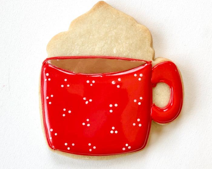 Image of While the red flood icing is still wet, use your white piping consistency icing to pipe small dots on the body of the mug. Doing this while the icing is wet will allow the white dots to blend into the red flood. If you wait for the red flood to dry, the white dots will stand proud of the red body of the mug.