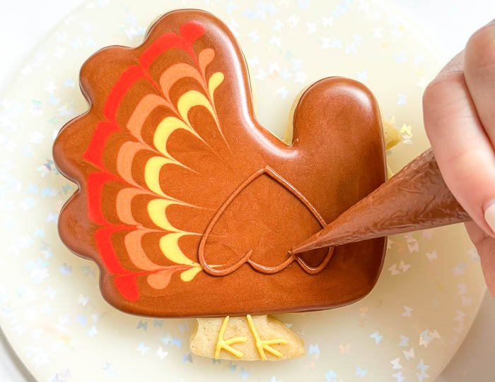 Image of Using the brown detail consistency icing, pipe the turkey's wing as shown. We'll be repeating the wet-on-wet technique used in steps 3-6 above to fill in the wing, so be sure to read ahead to be prepared to move quickly.