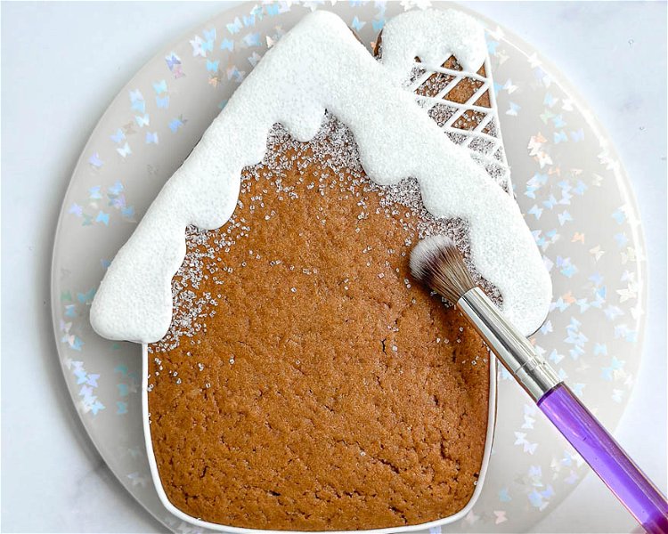 Image of Using the fluffy fresh, carefully brush away any excess sanding sugar from the cookie. Don't worry about getting every piece. A little snow on the house adds charm!