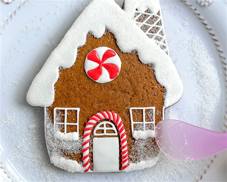 Image of Carefully transfer the cookie to the plate used for the sanding sugar. Sprinkle the sanding sugar on the snow sections you just piped and carefully brush the excess away using the small fluffy brush.