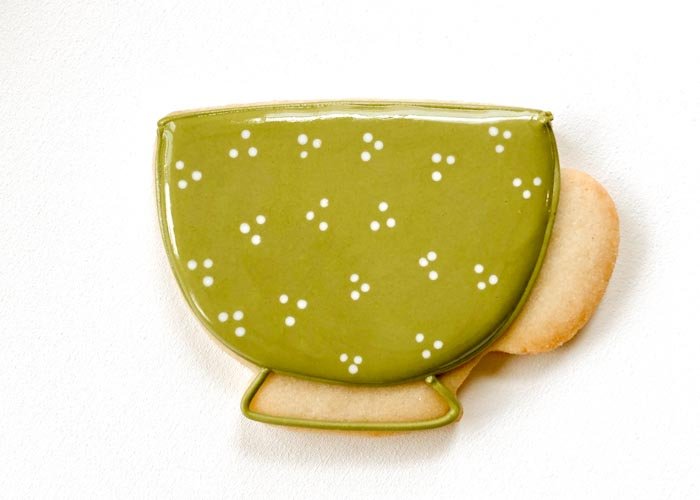Image of While the green flood icing is still wet, pipe some white dots in the body of the teacup. This is called a wet-on-wet technique, and the dots will blend into the green flood.