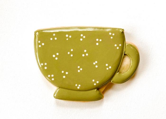 Image of Outline the handle of the teacup with green piping consistency icing, and then flood the base of the teacup and the handle of the teacup with green flood consistency icing. Allow this area to dry until just crusting over before moving to the next step. This may take up to 60 minutes. You can speed the process up by placing the cookies next to or under a fan set to a medium speed.