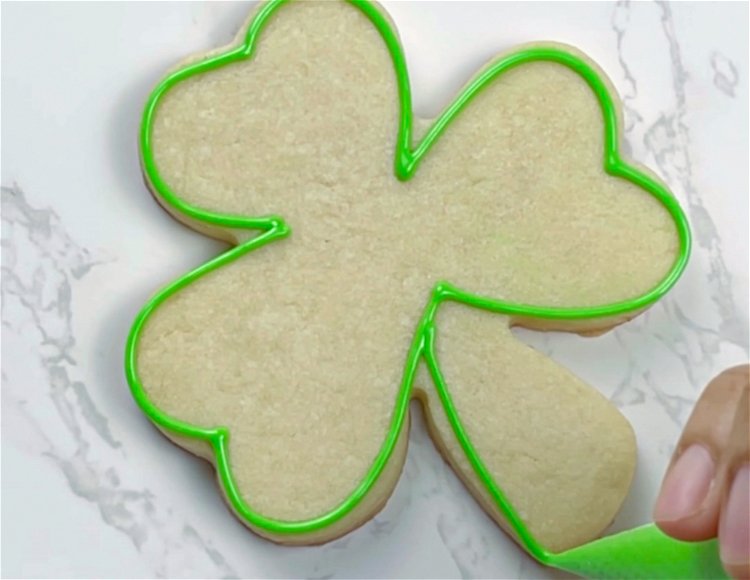 Image of Using the green piping/outline consistency icing, outline the stem of the shamrock. Outlining the stem separate from the leaves will create a nice differentiation between the two parts of the cookie.