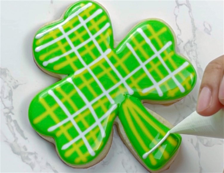 Image of Pipe three vertical lines and two horizontal lines of yellow icing on the stem of the shamrock.