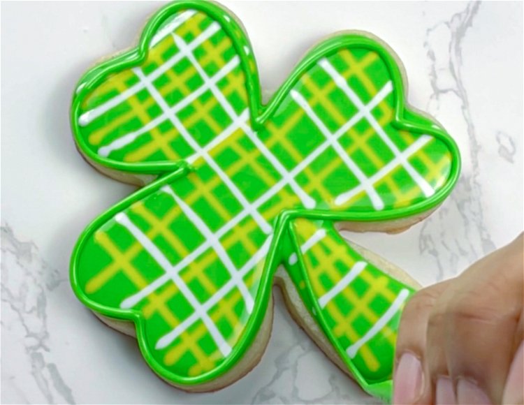 Image of Once your royal icing has just crusted over, outline first the leaves and then the stem of the shamrock with green piping consistency icing. This adds a bit more detail and definition to the cookie.