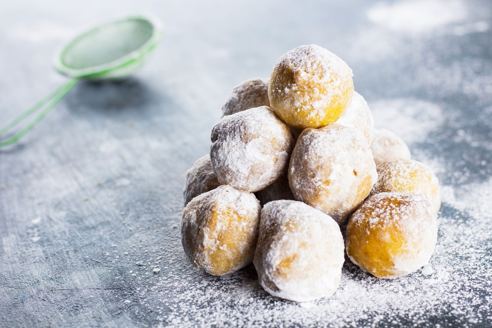Una pila de bocaditos de donut clásicos cubiertos con azúcar glas en una encimera gris.