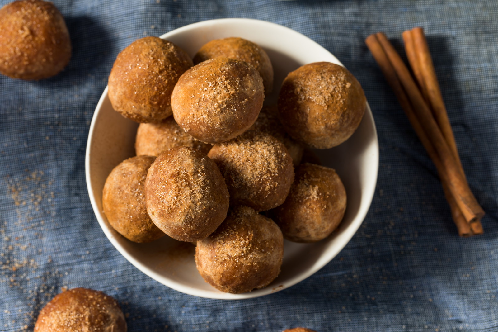 A white bowl of maple donut bites on a blue table cloth.