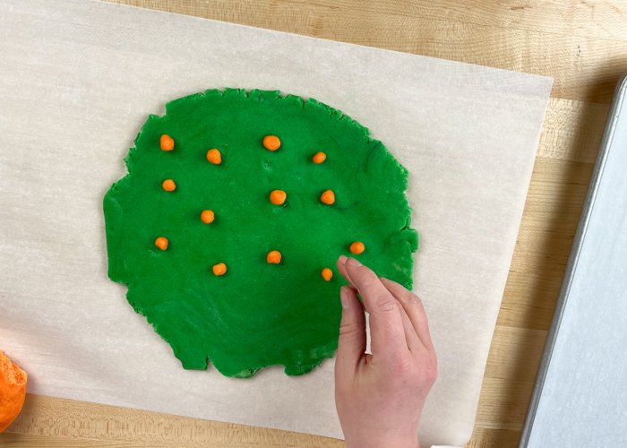 Image of Pinch off small amounts of orange dough and roll it into small balls. Gently press the balls into the green base dough. Keep in mind that the balls will become larger as you roll them out, so make them smaller than you want your dots to be.