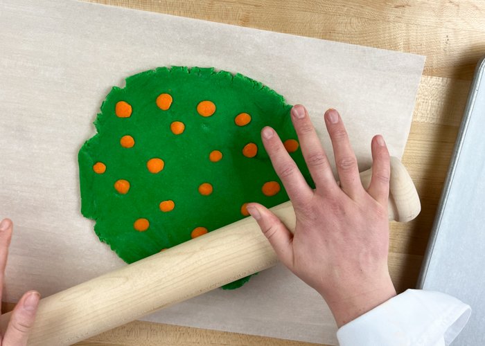 Image of Roll the orange dots into the green dough until they are well adhered to the green base.