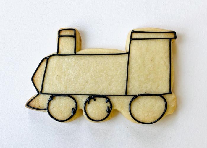 Image of Next, use black piping consistency icing to outline the wheels and cow catcher of the train. Add a window to the cab of the train with black piping consistency icing.