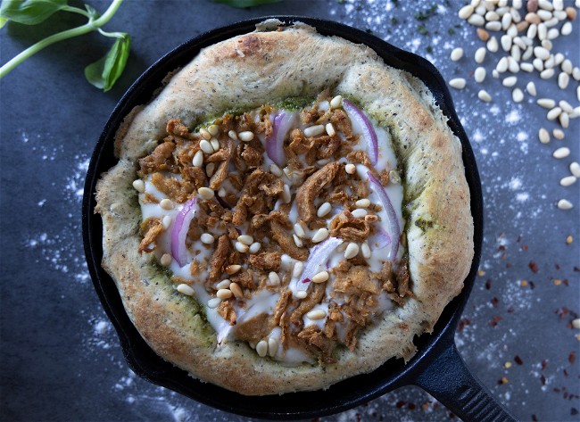 Naked Shredded Chicken Pesto Pizza in a cast iron skillet garnished with basil, pine nuts and crushed red pepper