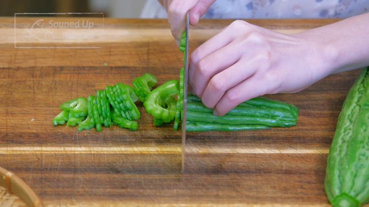 Image of Discard both ends of the bitter melon and cut it in halves lengthwise. Then, scrape the white spongy center using a spoon. Once it is clean, you can cut it into thin slices. 