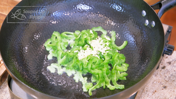 Image of Turn the heat to high and heat the wok until smoking hot. Add a big drizzle of oil and toss in the bitter melon and minced garlic. Stir for 2 minutes.