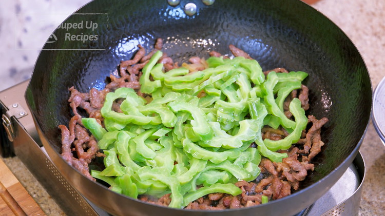 Image of Add garlic, julienned red chili, zhacai, and the blanched bitter melon. Continue to stir over high heat for 3 minutes to make sure the flavor of the zha cai is thoroughly distributed.