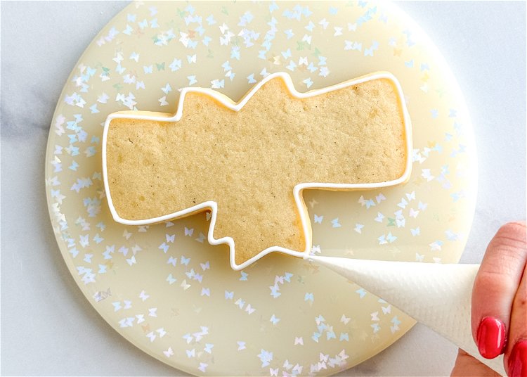 Image of Using the white outline consistency icing, outline the entire cookie shape. 