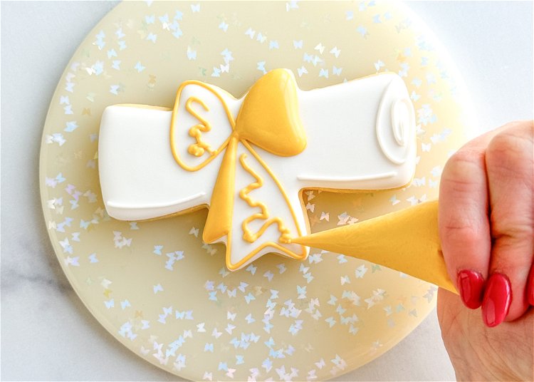 Image of Once the two sections of the yellow bow have crusted over, repeat step 6 on the remaining two sections, piping a squiggle of yellow outline consistency icing in the center of each of the two remaining sections.  