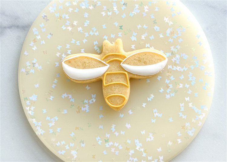 Image of Using the yellow outline consistency icing, outline the three sections of the bee, as shown in the photo. 