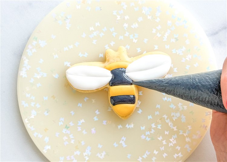 Image of Once the yellow and white sections have dried for at least one hour, pipe the remaining sections of the bee using the black outline consistency icing. Smooth out the icing with your scribe tool or toothpick.  