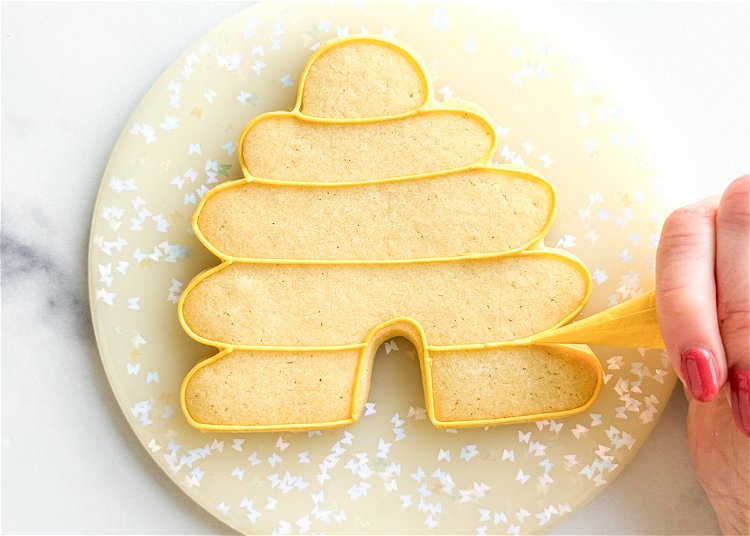 Image of Using the yellow outline consistency icing, outline the cookie shape and the elongated ovals of the beehive design. Outlining each of these separately will create good definition between the areas. 