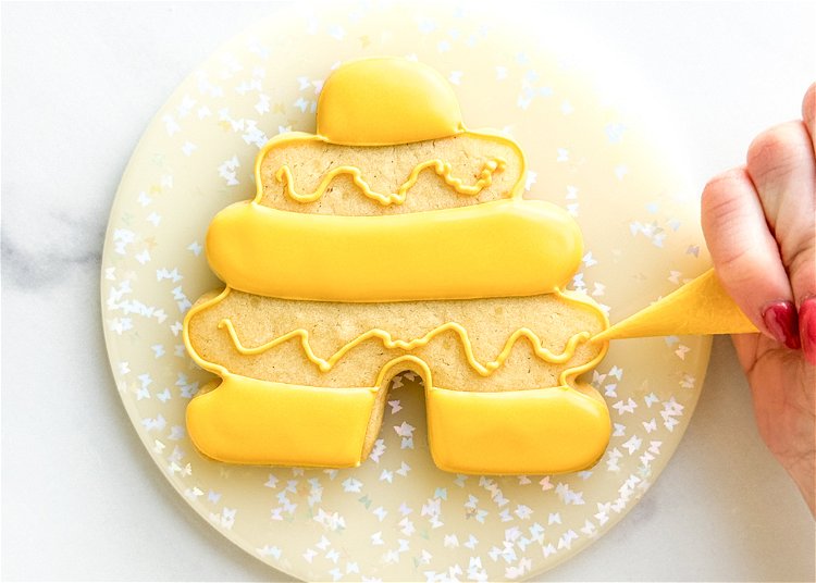 Image of Once the flooded sections of the beehive cookie have crusted over or dried, repeat step 3, piping a squiggle of yellow outline consistency icing in the middle of the empty sections. 